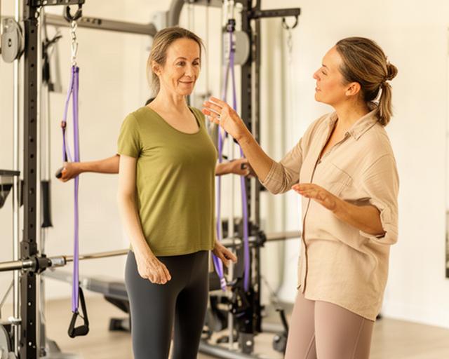Fitness coach guiding an adult through a movement assessment beside training equipment
